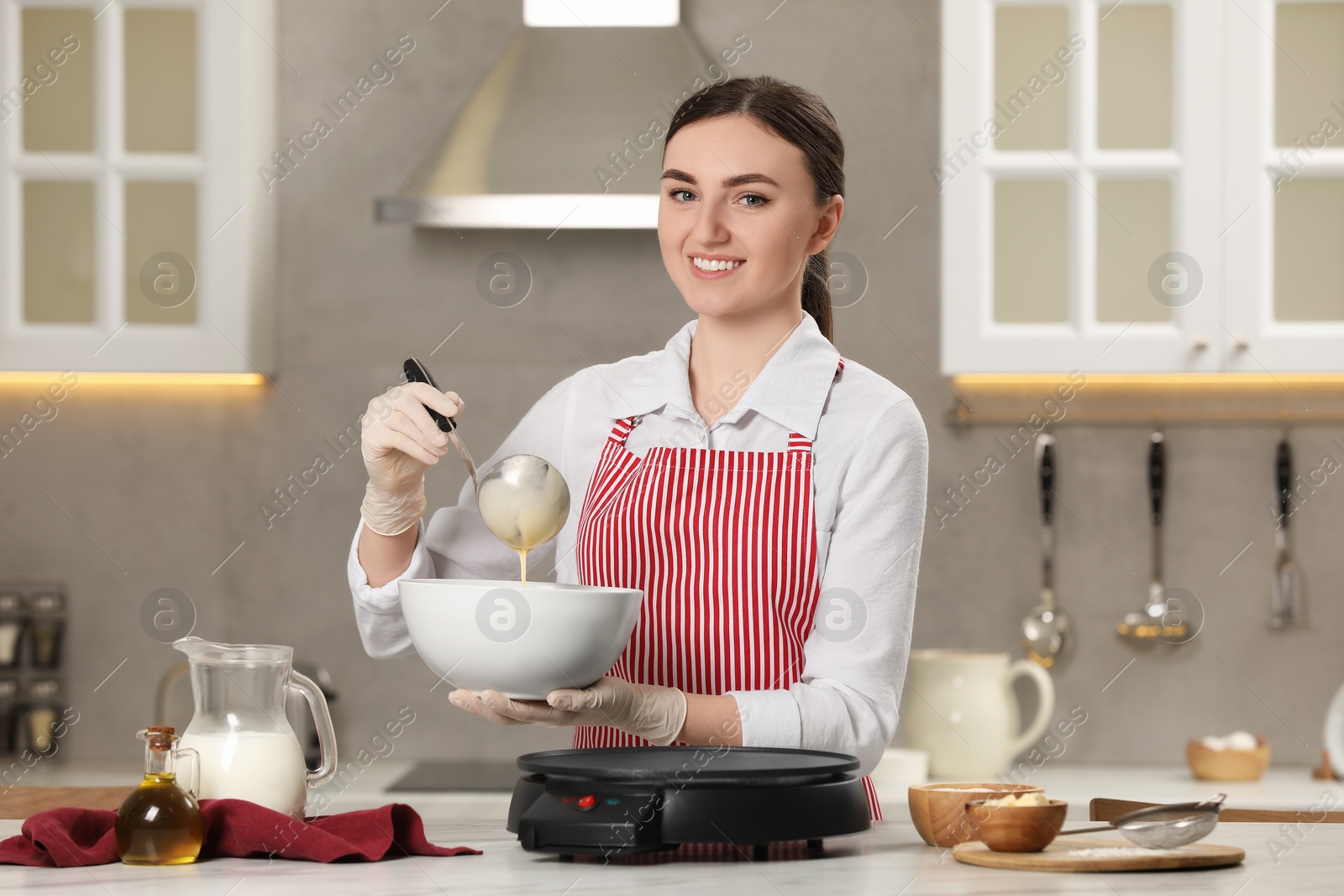 Photo of Young woman cooking delicious crepes in kitchen