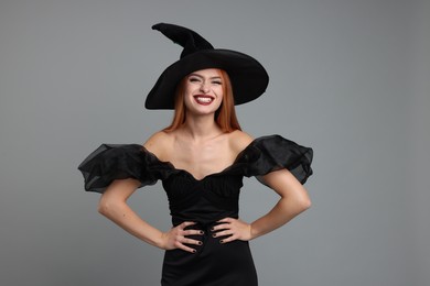 Photo of Happy young woman in scary witch costume on light grey background. Halloween celebration