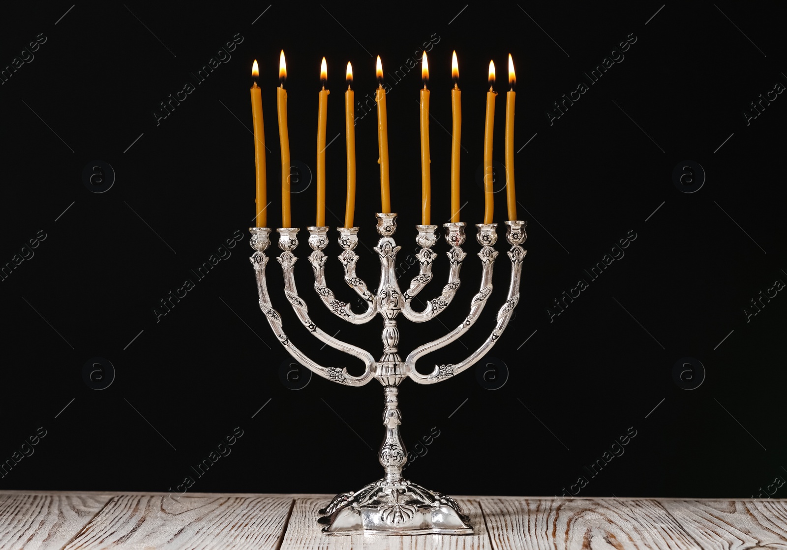 Photo of Silver menorah with burning candles on table against black background. Hanukkah celebration