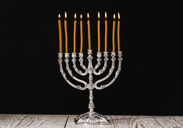 Photo of Silver menorah with burning candles on table against black background. Hanukkah celebration