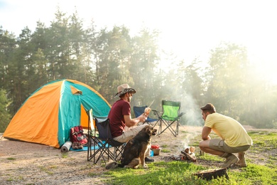 People cooking on bonfire near camping tent in wilderness