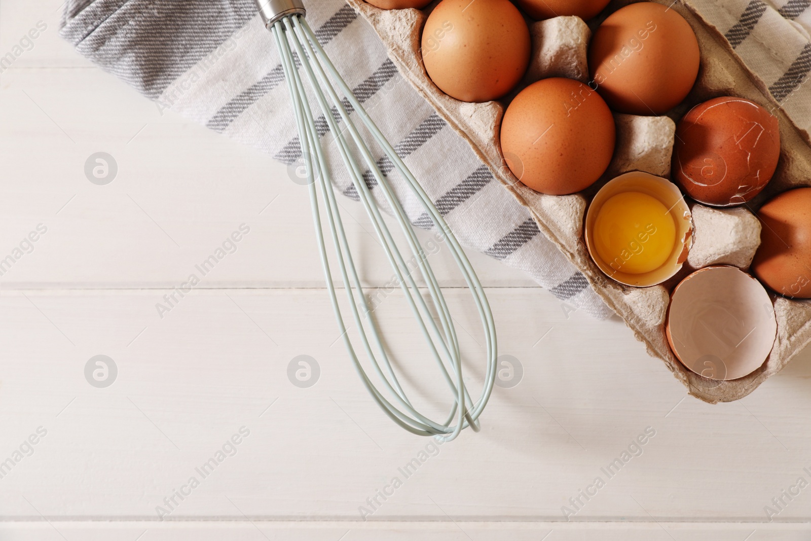 Photo of Fresh raw chicken eggs and whisk on white wooden table, flat lay. Space for text