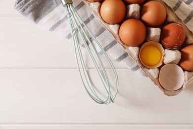 Fresh raw chicken eggs and whisk on white wooden table, flat lay. Space for text