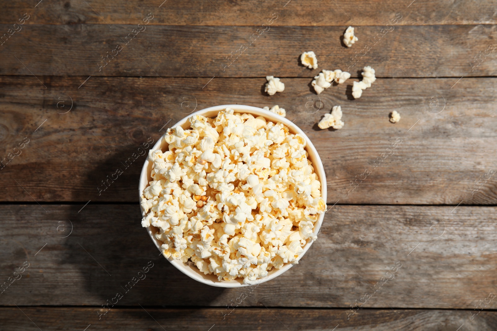 Photo of Cup with fresh tasty popcorn on wooden background, top view. Cinema snack