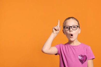 Photo of Portrait of cute girl in glasses on orange background. Space for text