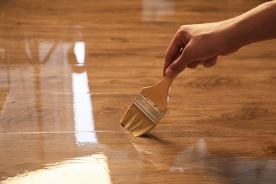 Photo of Woman with brush varnishing wooden surface, closeup