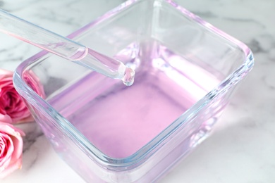 Dripping rose essential oil into glass bowl on table, closeup