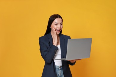 Emotional young woman with modern laptop on yellow background