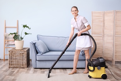 Young woman hoovering carpet with vacuum cleaner in living room