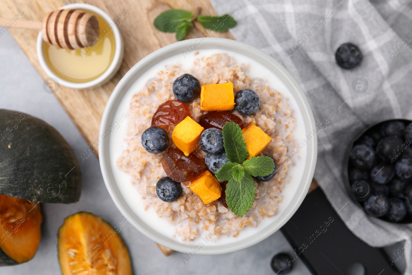 Photo of Tasty wheat porridge with pumpkin, dates and blueberries in bowl on table, flat lay
