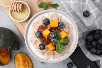 Tasty wheat porridge with pumpkin, dates and blueberries in bowl on table, flat lay