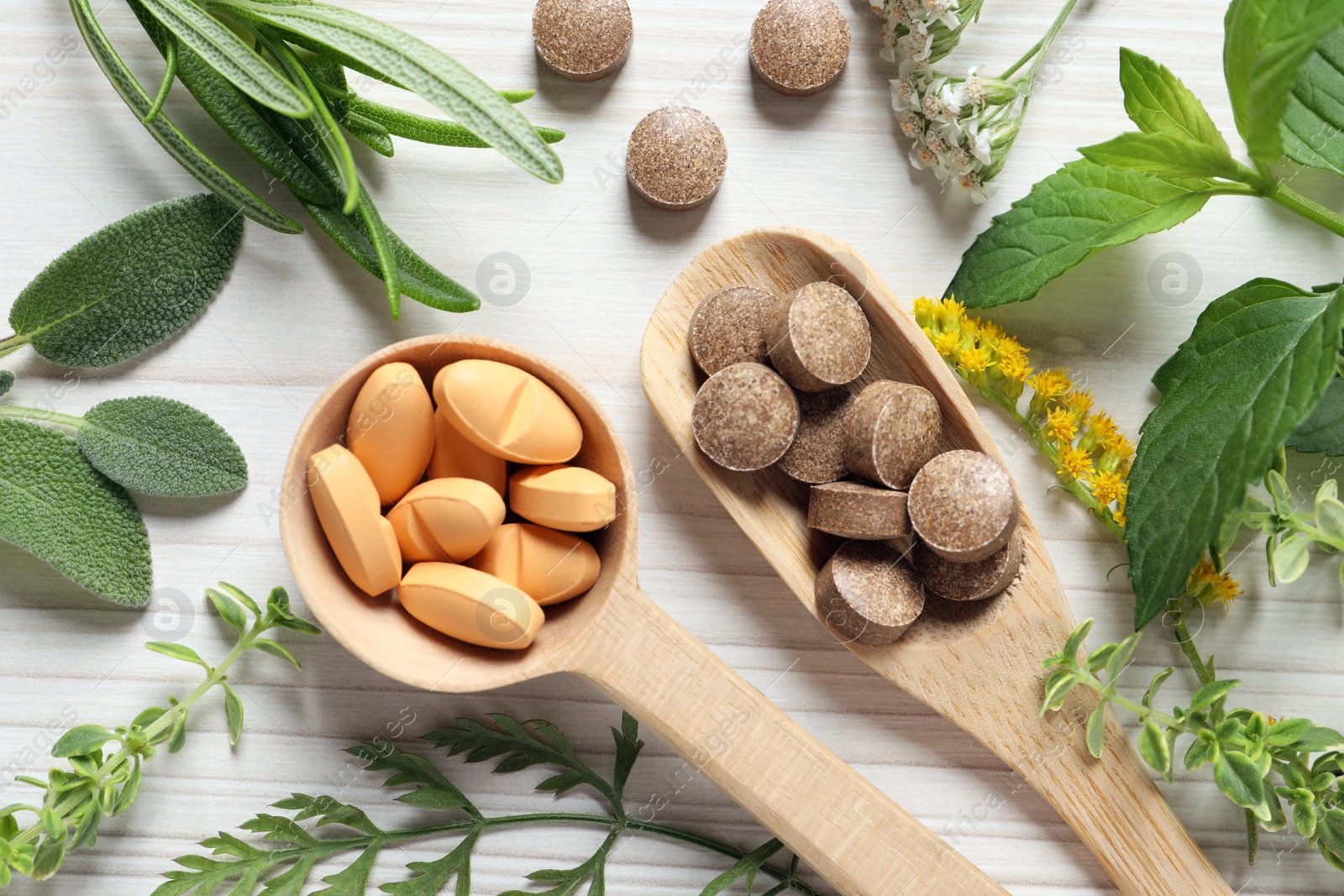 Photo of Different pills, herbs and flowers on white wooden table, flat lay. Dietary supplements