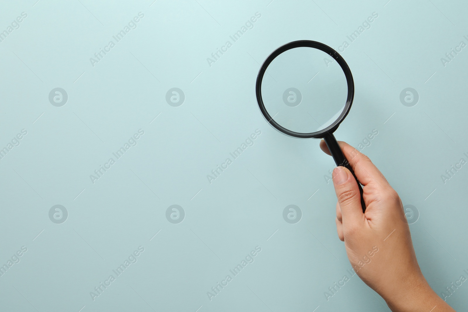 Photo of Woman holding magnifying glass on light blue background, closeup with space for text. Microbes concept