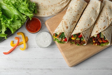 Board with delicious meat tortilla wraps on white wooden table, flat lay