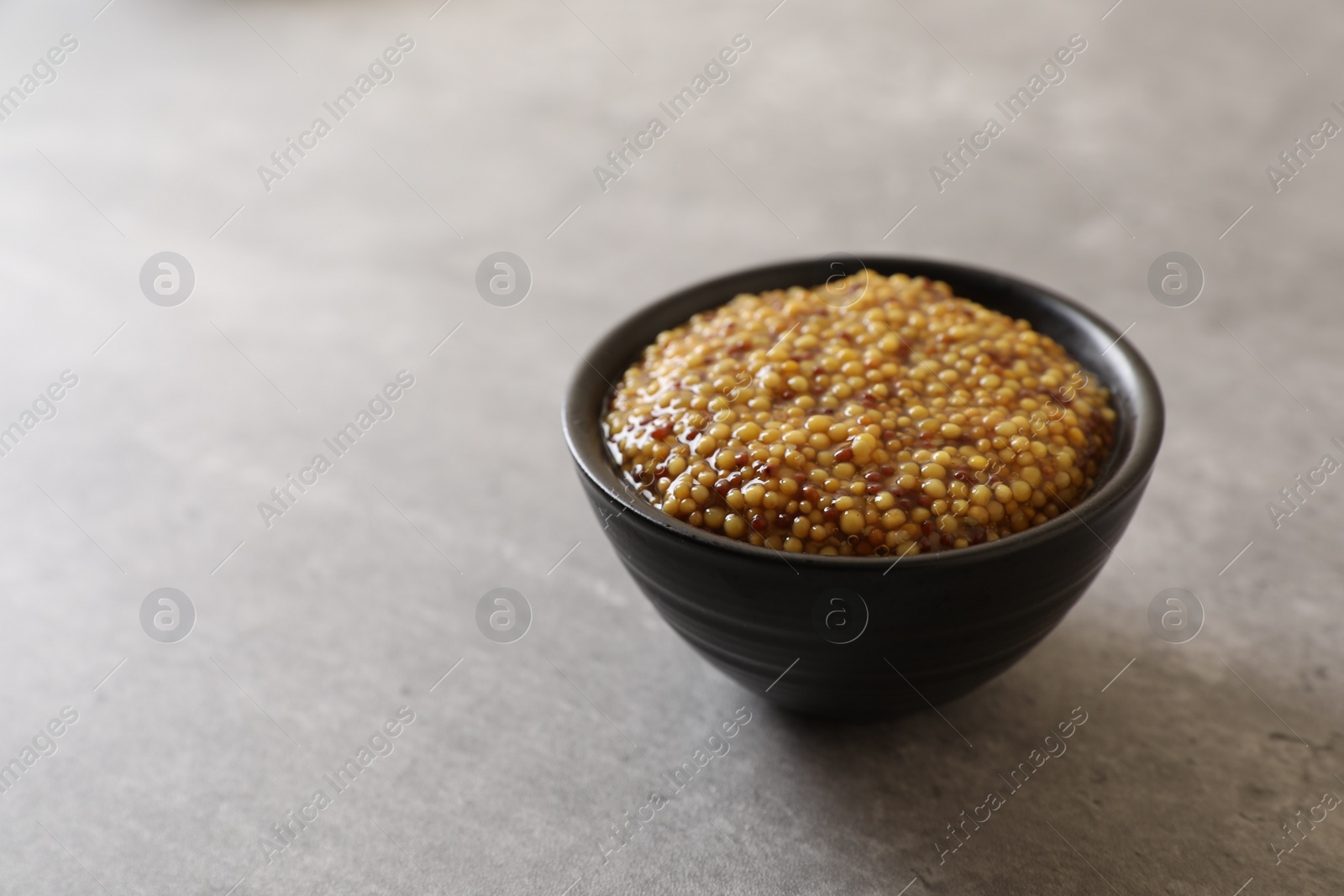Photo of Bowl of whole grain mustard on grey table, space for text