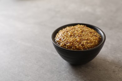 Bowl of whole grain mustard on grey table, space for text