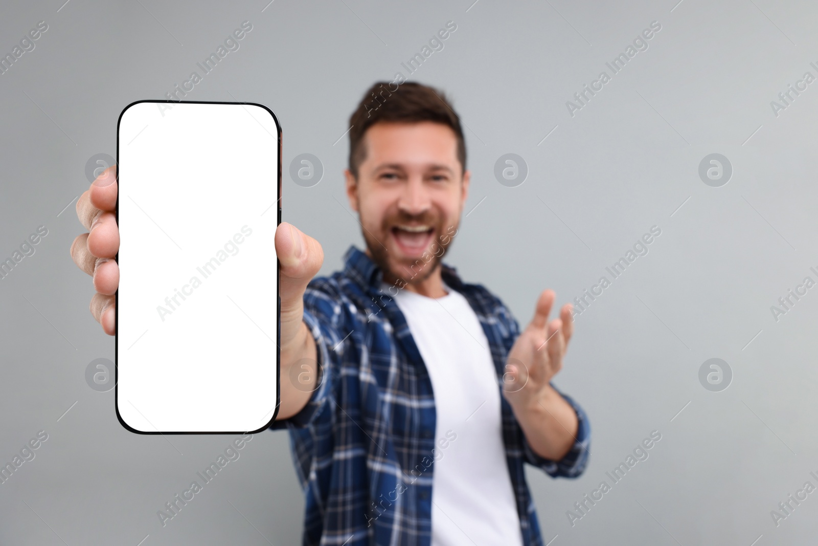 Photo of Surprised man showing smartphone in hand on light grey background, selective focus. Mockup for design