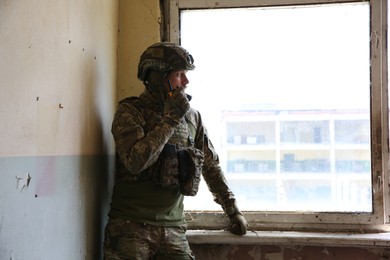 Photo of Military mission. Soldier in uniform with radio transmitter inside abandoned building, space for text