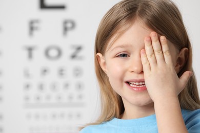 Photo of Little girl covering her eye against vision test chart