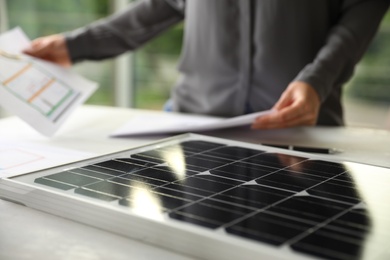 Photo of Solar panel and blurred person with papers on background, closeup