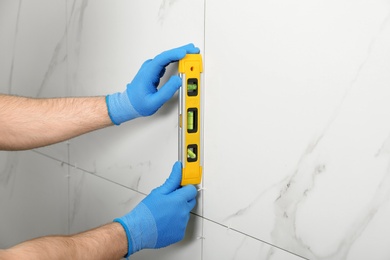 Man checking proper ceramic tile installation with level on wall, closeup. Building and renovation works