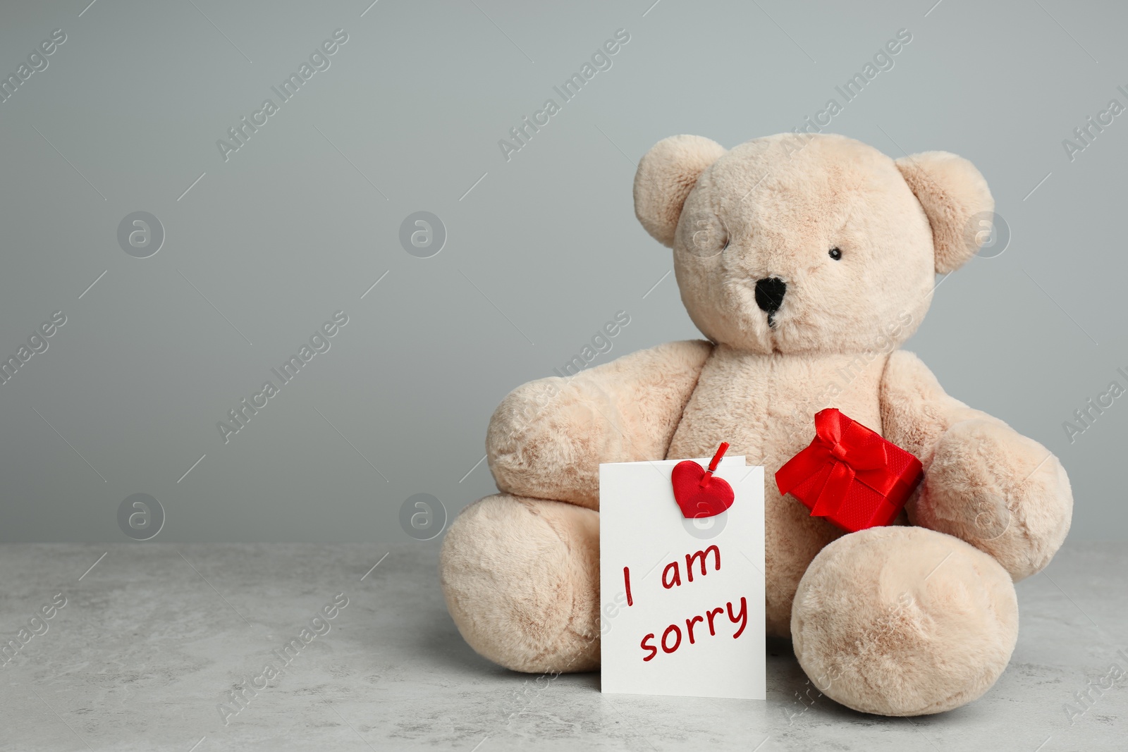 Image of Apology. Cute teddy bear with gift box and I Am Sorry card on grey textured table, space for text