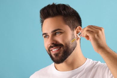 Handsome man applying cosmetic serum onto face on light blue background, space for text