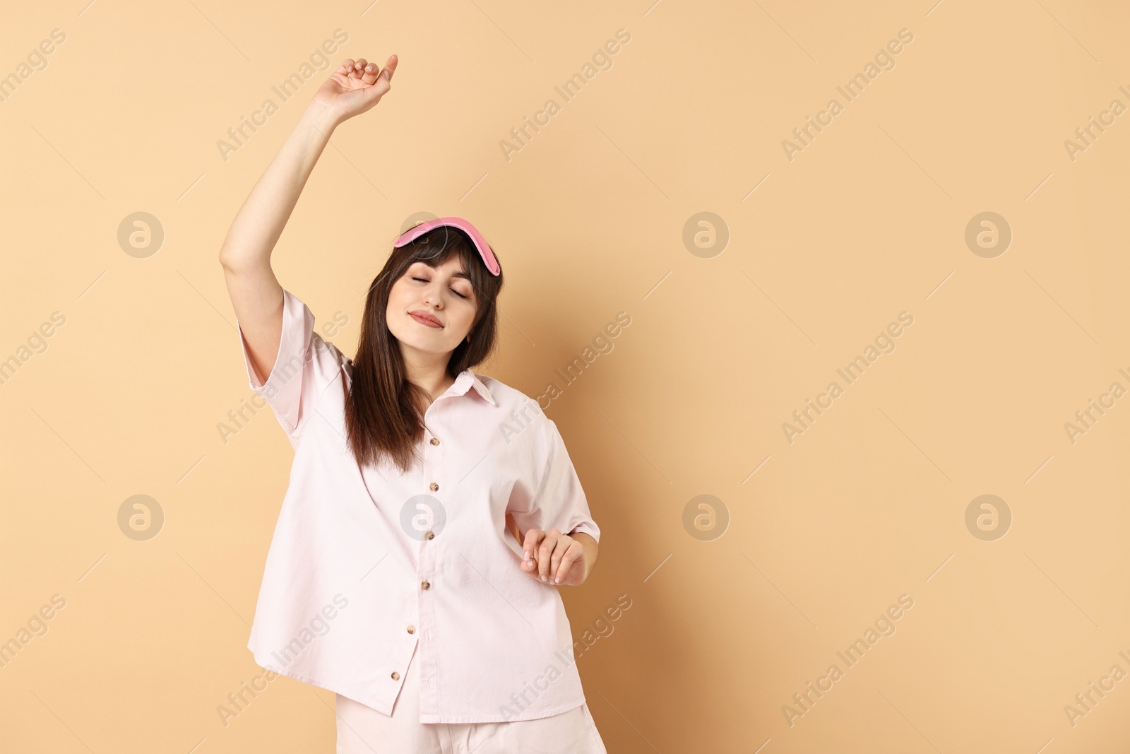 Photo of Woman in pyjama and sleep mask stretching on beige background, space for text