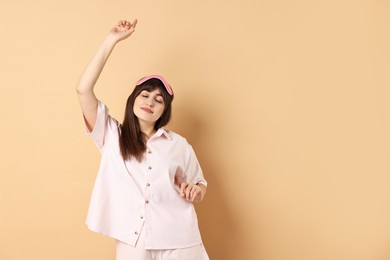 Woman in pyjama and sleep mask stretching on beige background, space for text