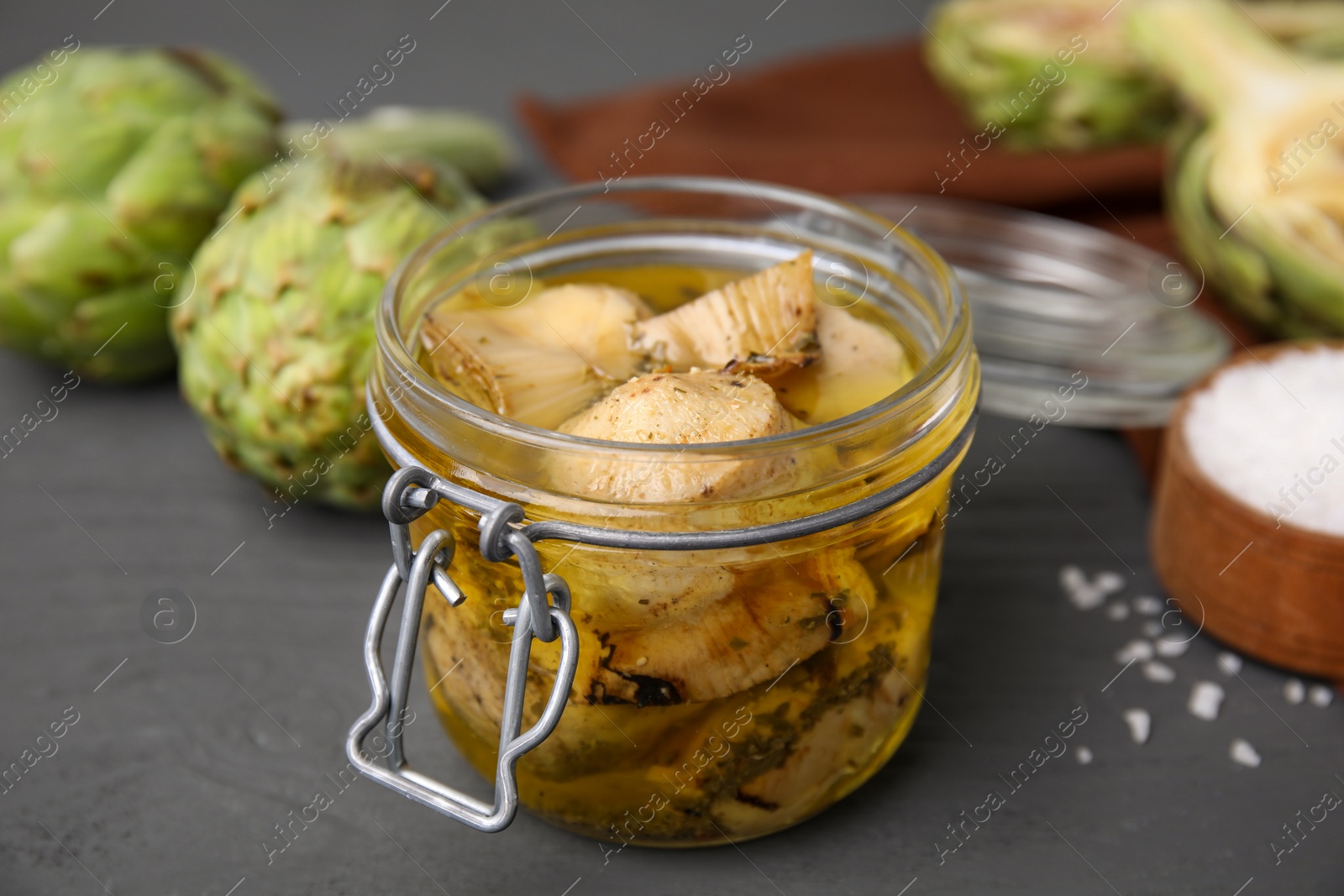 Photo of Jar of delicious artichokes pickled in olive oil on grey table, closeup