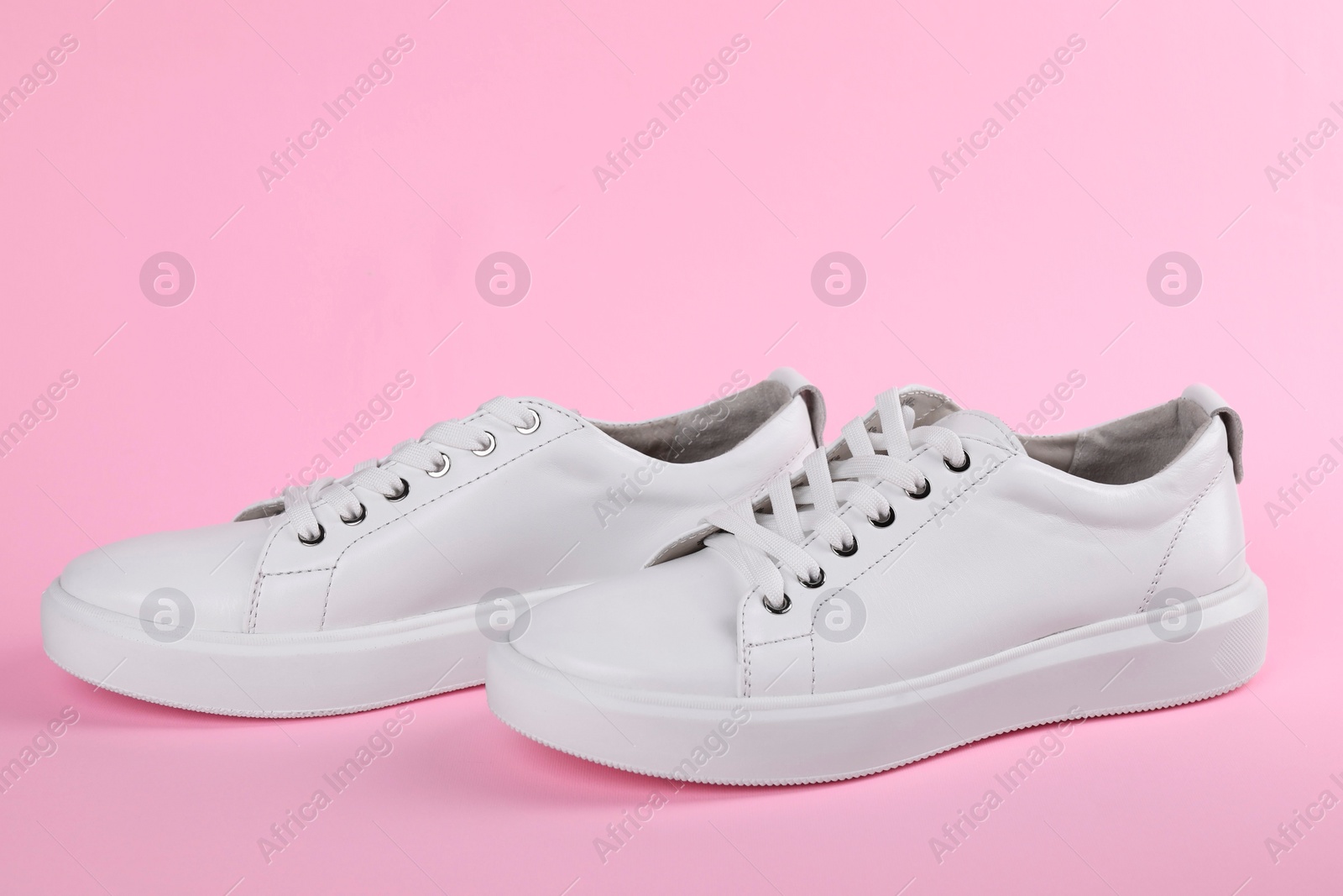 Photo of Pair of stylish white sneakers on pink background