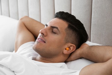 Man with foam ear plugs sleeping in bed