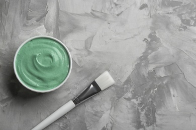 Photo of Spirulina facial mask and brush on grey table, flat lay. Space for text