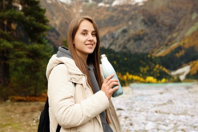 Photo of Happy young woman holding thermo bottle with drink in beautiful mountains. Space for text