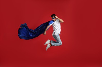 Man in superhero cape and mask jumping on red background
