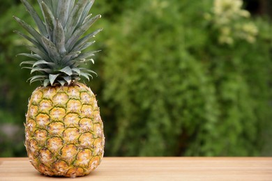 Delicious ripe pineapple on wooden table outdoors, space for text