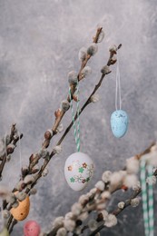 Photo of Beautiful willow branches with painted eggs on light grey background, closeup. Easter decor