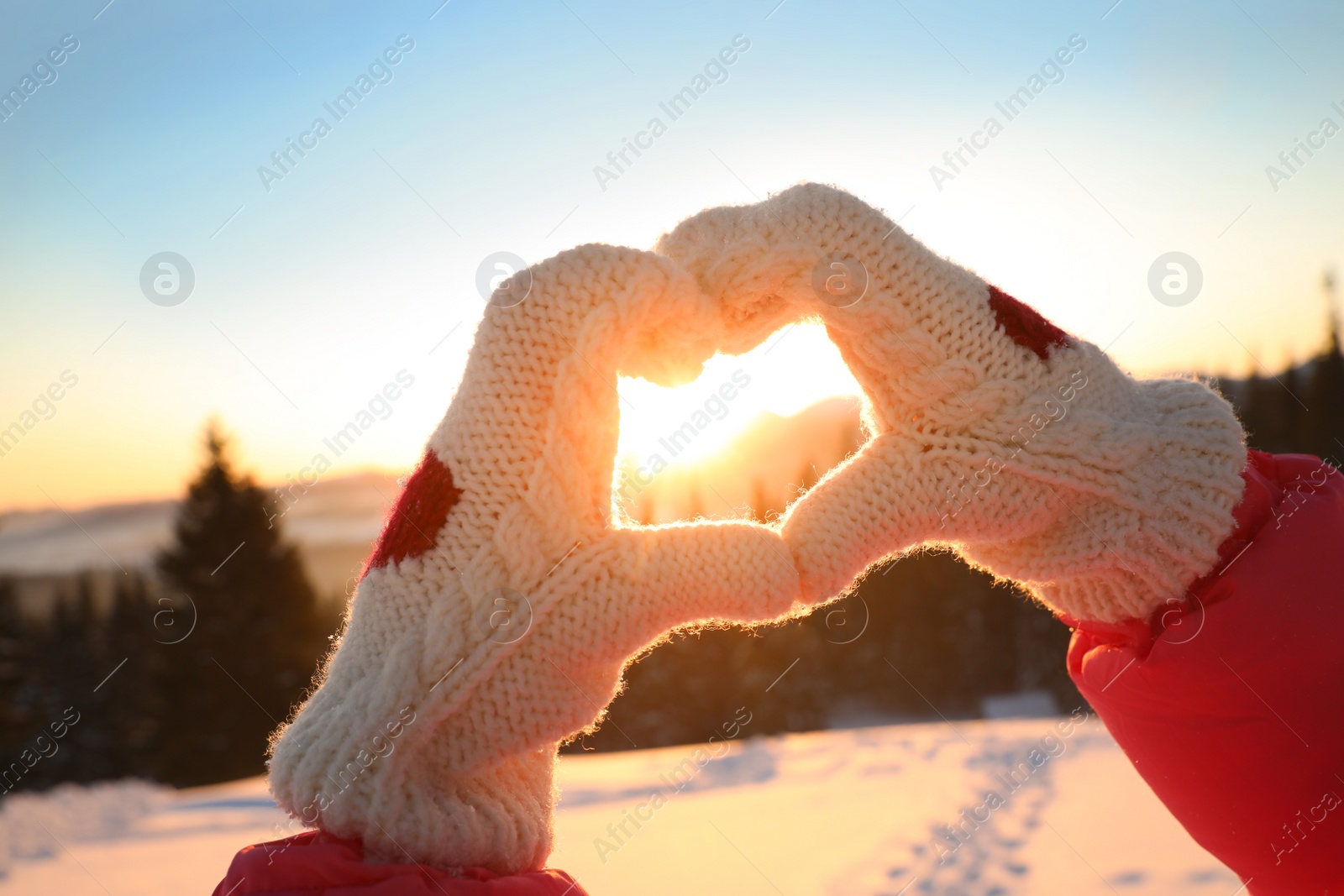 Photo of Woman making heart with hands outdoors at sunset, closeup. Winter vacation