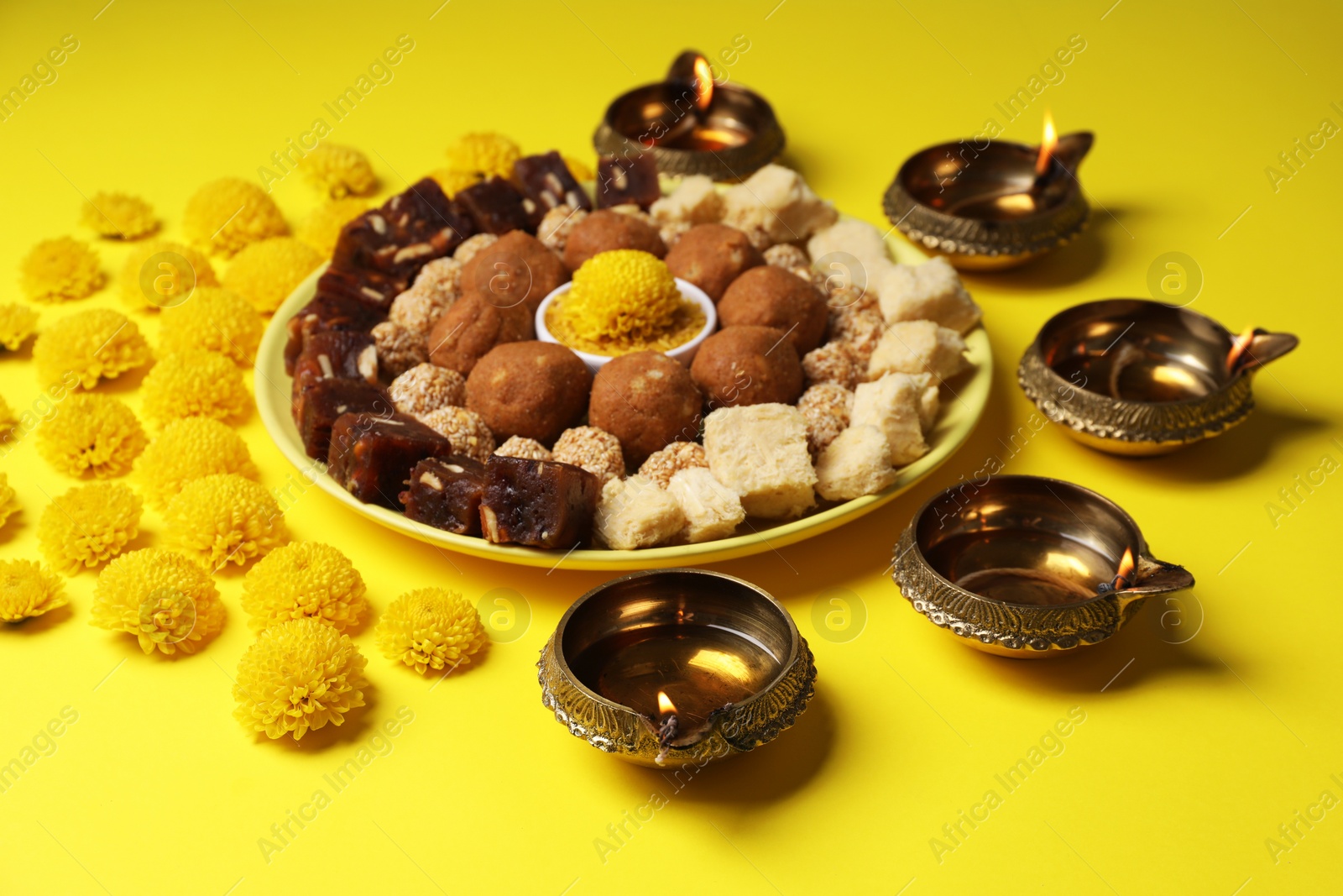 Photo of Happy Diwali. Composition with diya lamps, chrysanthemum flowers and delicious Indian sweets on yellow table