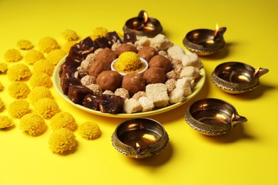 Photo of Happy Diwali. Composition with diya lamps, chrysanthemum flowers and delicious Indian sweets on yellow table