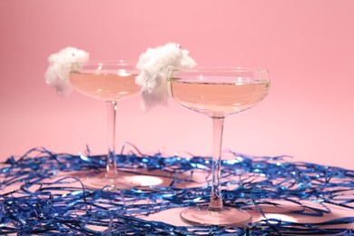 Tasty cocktails in glasses decorated with cotton candy and blue shiny streamers on pink background