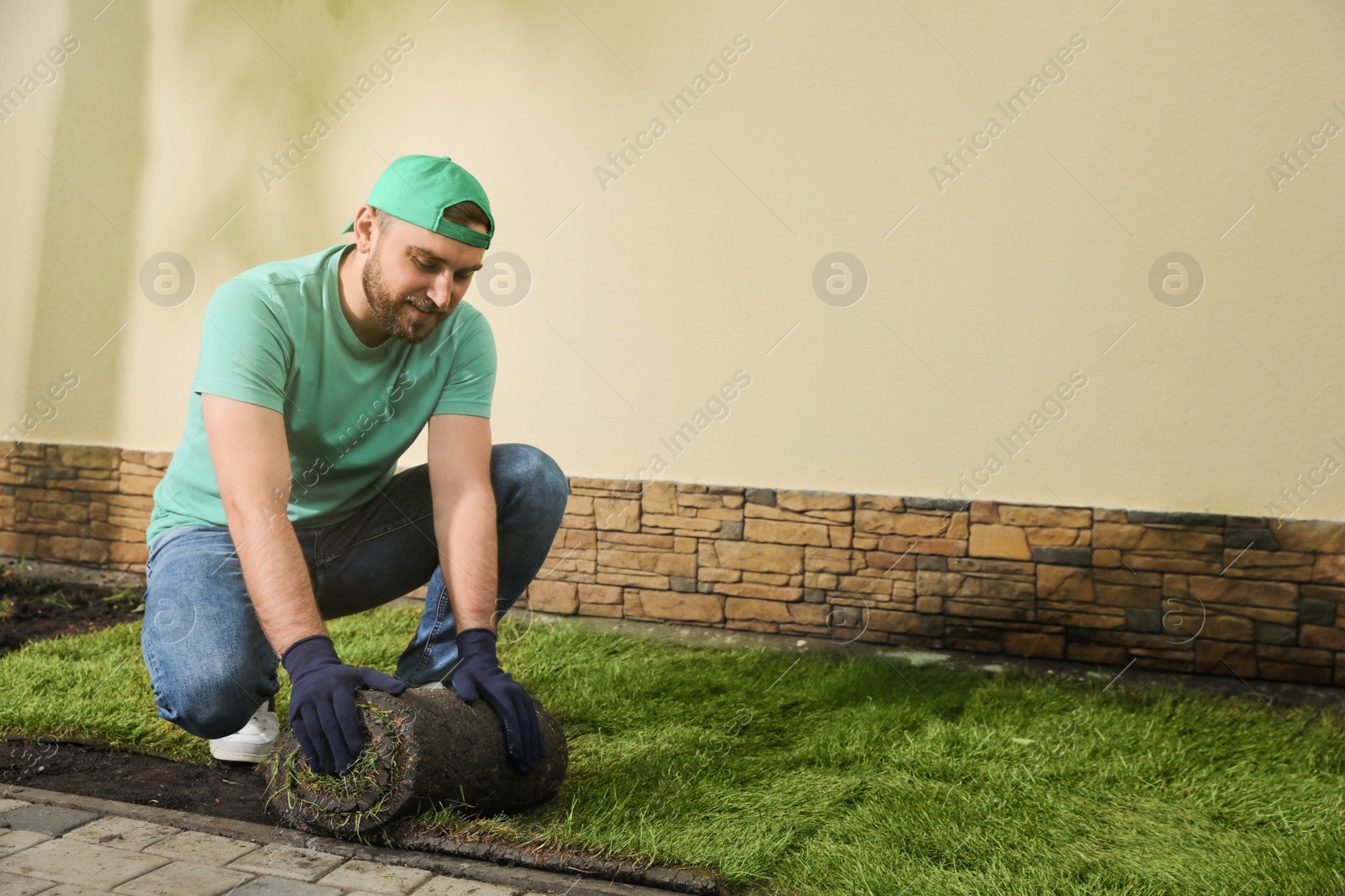 Photo of Worker laying grass sod on ground at backyard, space for text