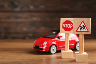 Photo of Miniature road signs and car on wooden table, space for text. Driving school