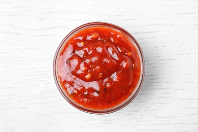 Photo of Bowl of hot chili sauce on white wooden background, top view