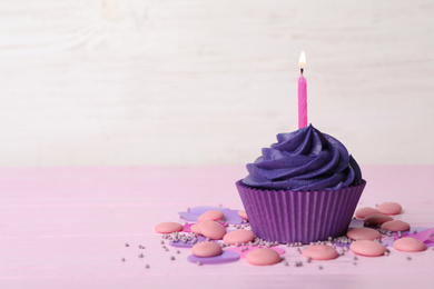Delicious birthday cupcake with cream and burning candle on pink table. Space for text