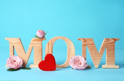 Word "MOM" made of wooden letters and flowers on color background. Happy Mother's Day