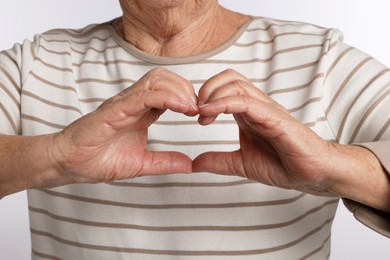 Photo of Elderly woman making heart with her hands on white background, closeup