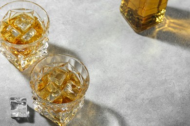Photo of Whiskey in glasses with ice cubes on grey textured table, above view. Space for text