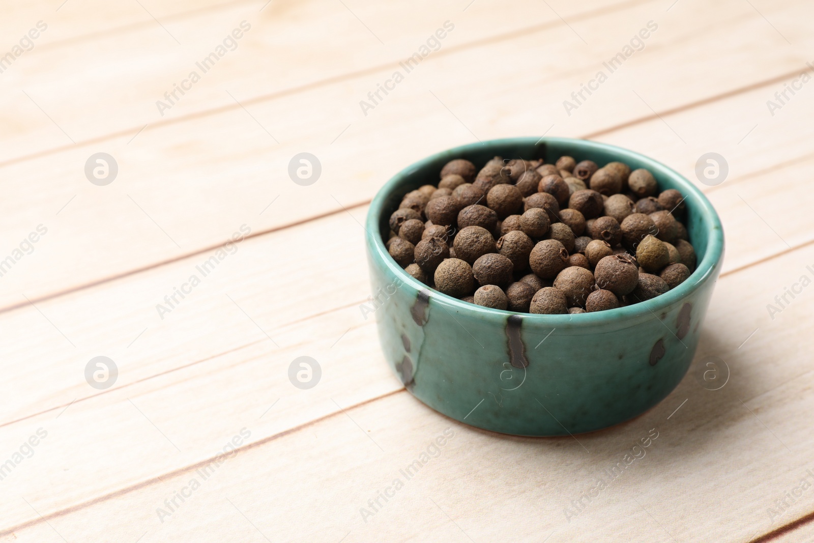 Photo of Dry allspice berries (Jamaica pepper) in bowl on light wooden table, space for text