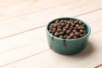 Dry allspice berries (Jamaica pepper) in bowl on light wooden table, space for text